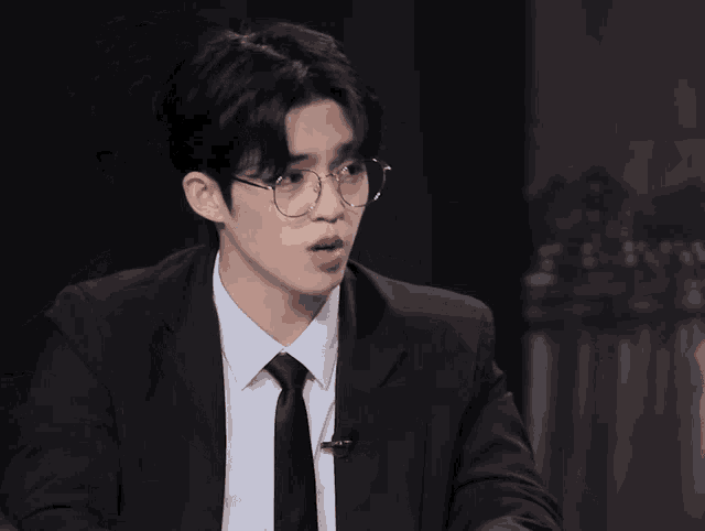 a man wearing glasses and a suit points at his watch