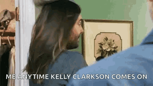a man with long hair and a beard is standing next to a woman in front of a picture .