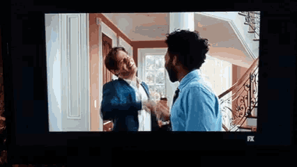 two men are standing next to each other in a room on a television screen .