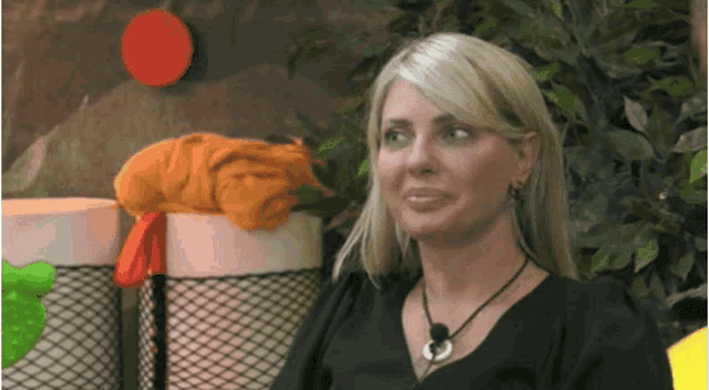 a blonde woman wearing a black shirt and a necklace looks at the camera