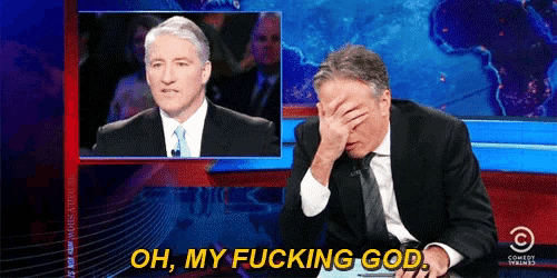 a man in a suit and tie is covering his face with his hand while another man looks on and says oh my fucking god