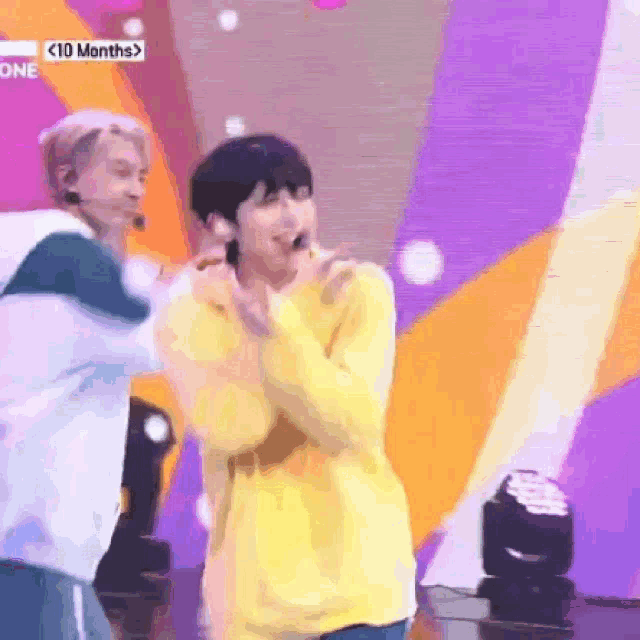 a man in a yellow sweater is standing on a stage with a microphone .