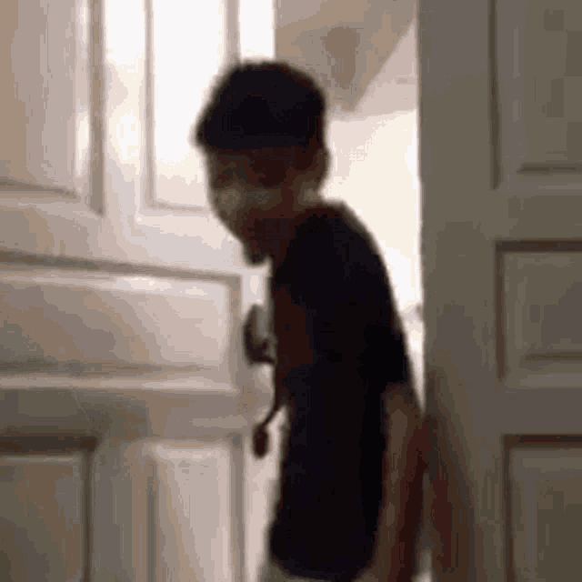 a young boy is standing in front of a door and looking out .