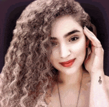 a woman with long curly hair has a tattoo of a treble clef on her wrist