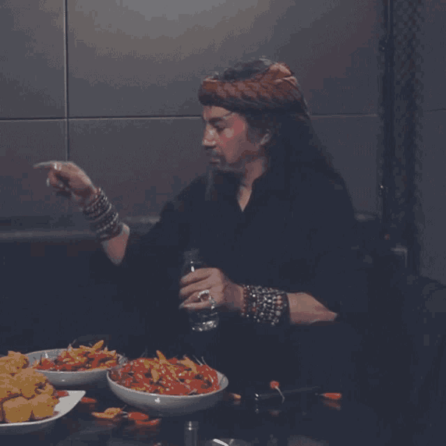 a man in a turban sits at a table with bowls of food and a bottle of water
