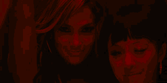 two women are standing next to each other in a dark room with a red background