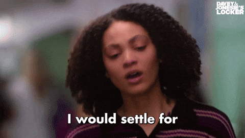 a woman with curly hair is saying `` i would settle for '' while standing in a hallway .