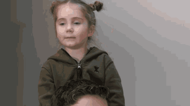 a little girl wearing a green jacket with a black x on it