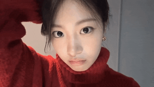 a woman wearing a red turtleneck sweater and earrings looks at the camera