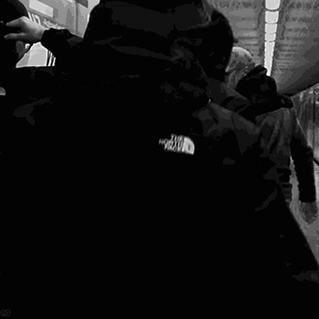 a group of people are standing in front of a wall and one of them is wearing a north face jacket .