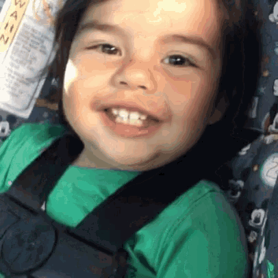 a young boy is wearing a green shirt and a black seat belt .