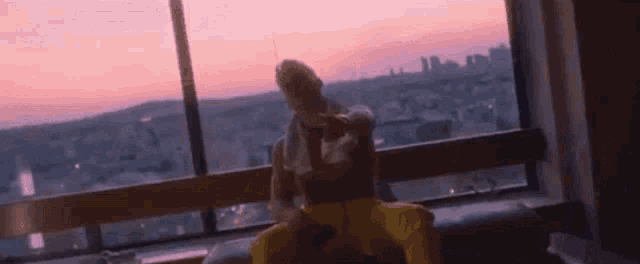 a man is sitting on a couch in front of a large window with a view of a city at sunset .