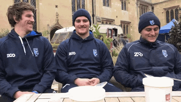 three men wearing zoo sweatshirts sit at a picnic table