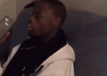 a man is sitting on a couch talking on a cell phone while wearing a white hoodie .