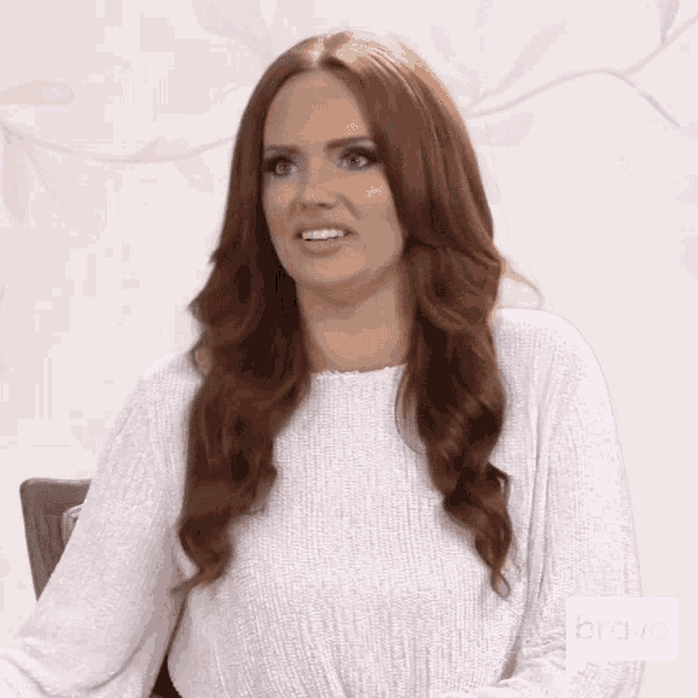 a woman with red hair wearing a white sweater is making a funny face .