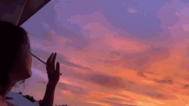 a person is smoking a cigarette in front of a cloudy sky at sunset .