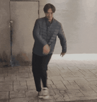 a man wearing a blue jacket and black pants is walking on a sidewalk