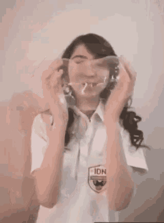 a woman in a school uniform is holding a condom in front of her face .