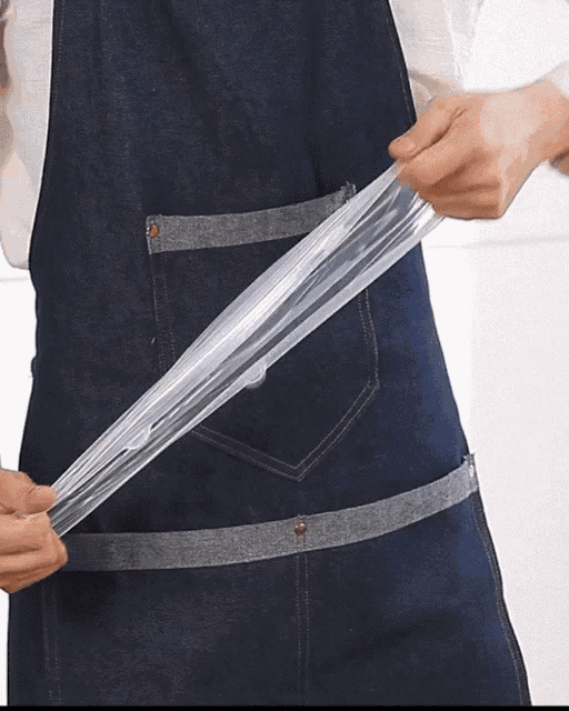 a person wearing a denim apron holds a clear plastic bag