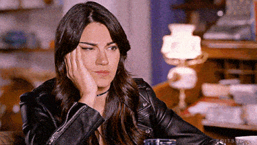a woman in a black leather jacket is sitting on a couch with her hand on her forehead .