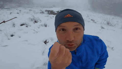 a man wearing a blue and orange adidas beanie stands in the snow
