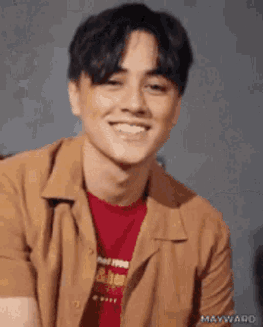 a young man wearing a tan shirt and a red shirt is smiling .