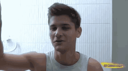 a young man in a tank top is standing in a bathroom .
