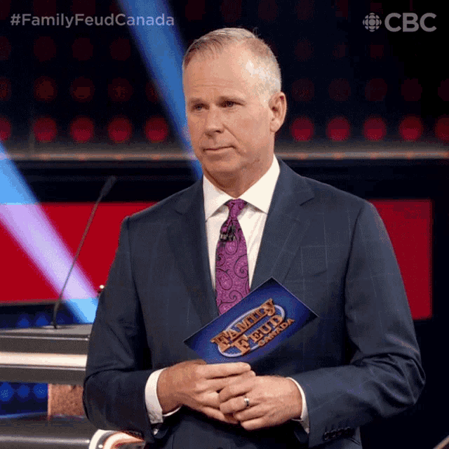 a man in a suit and tie holds a family feud canada sign