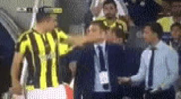a man in a yellow and black striped shirt is touching another man 's face .