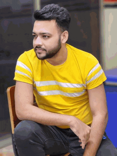 a man with a beard wearing a yellow shirt is sitting in a chair