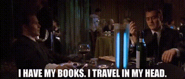 a man sitting at a table with a bottle of wine says i have my books i travel in my head ..