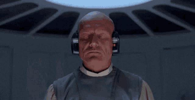 a bald man wearing headphones is looking at the camera in a dark room .