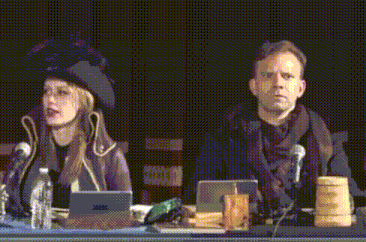 a man and a woman sitting at a table with microphones