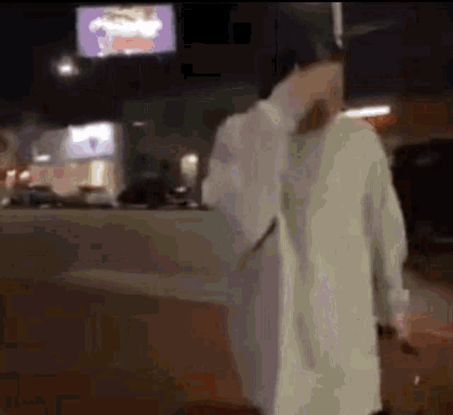 a man in a white coat is walking down a street at night with a suitcase .