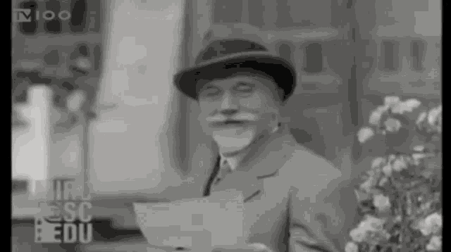 a man in a hat is holding a piece of paper in front of a sign that says tv100