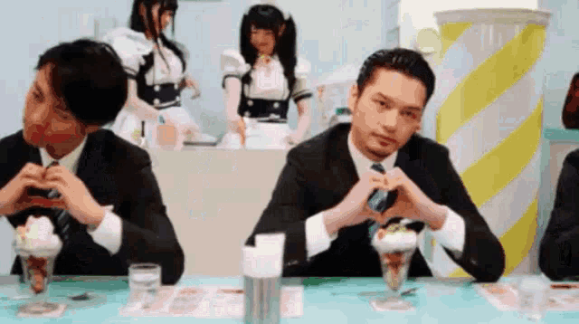 a man in a suit making a heart shape with his hands