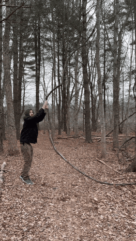 a man in a black jacket is holding a rope in a forest