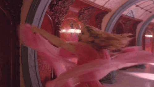 a woman in a pink dress is dancing in a room and laughing .
