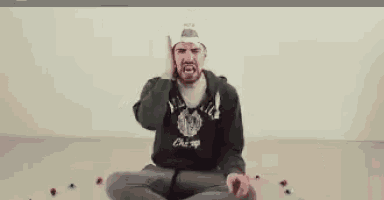a man with a beard is sitting on the floor with his hands on his ears .
