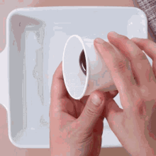 a person is holding a small cup in their hands in front of a white container .