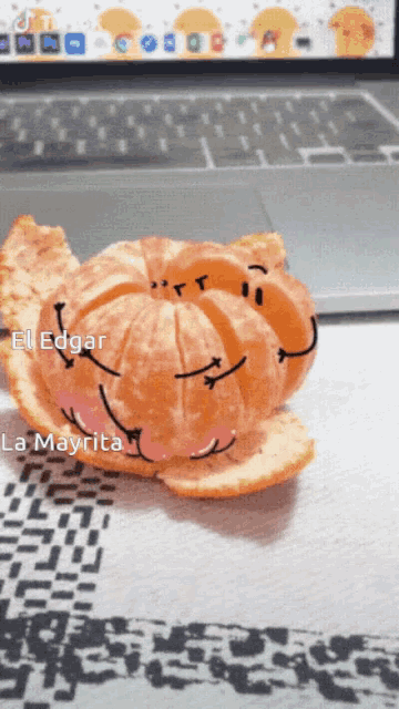 an orange with faces drawn on it sits in front of a laptop keyboard