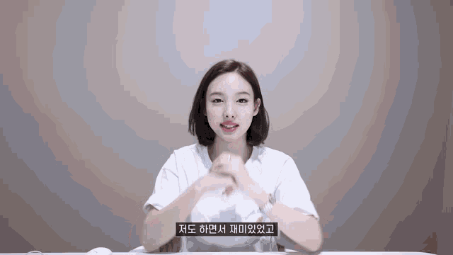 a woman in a white t-shirt is sitting at a table with her hands folded