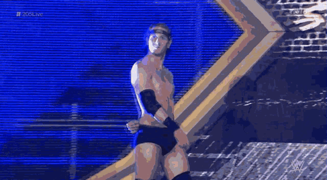 a shirtless wrestler stands in front of a brick wall with the hashtag # 20live on the bottom