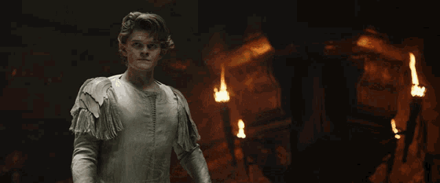 a man in a white shirt is standing in a dark room with fires