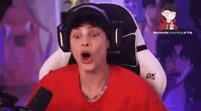 a man wearing headphones and a red shirt is sitting in a chair with his mouth open .