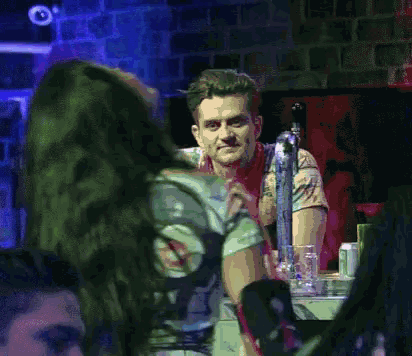 a man and a woman are sitting at a table in a bar . the man is wearing a bandana .