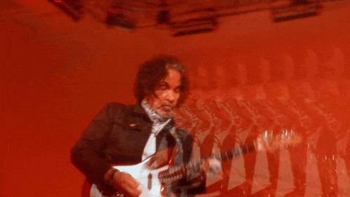 a man playing a guitar in front of a red background with a reflection of him