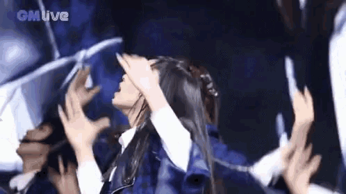 a woman is covering her face with her hands while a crowd of people reach for her .