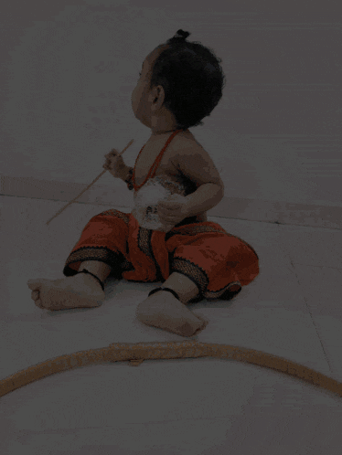 a baby sitting on the floor holding a stick and a bow