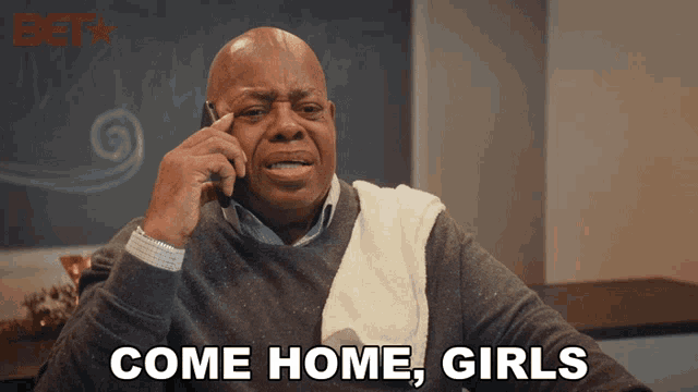 a man talking on a cell phone with the words come home girls behind him